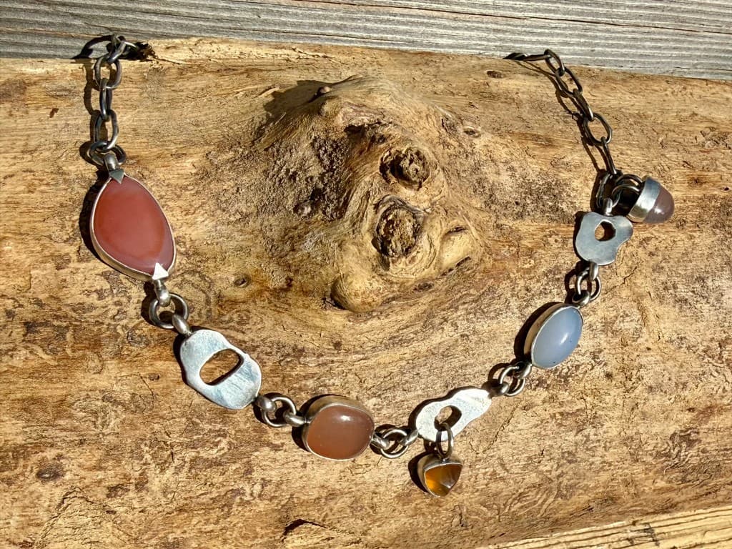 Oxidized silver link necklace with terracotta, periwinkle, and amber stones on weathered driftwood