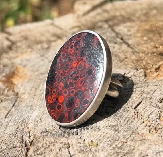 Handmade silver ring with a red patterned cabochon stone on weathered wood