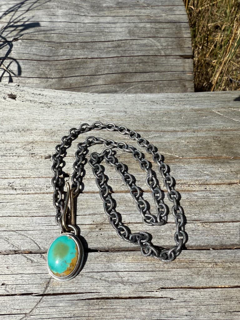 Chunky oxidized silver chain with a large turquoise pendant and brass shepherd hook clasp on weathered wood