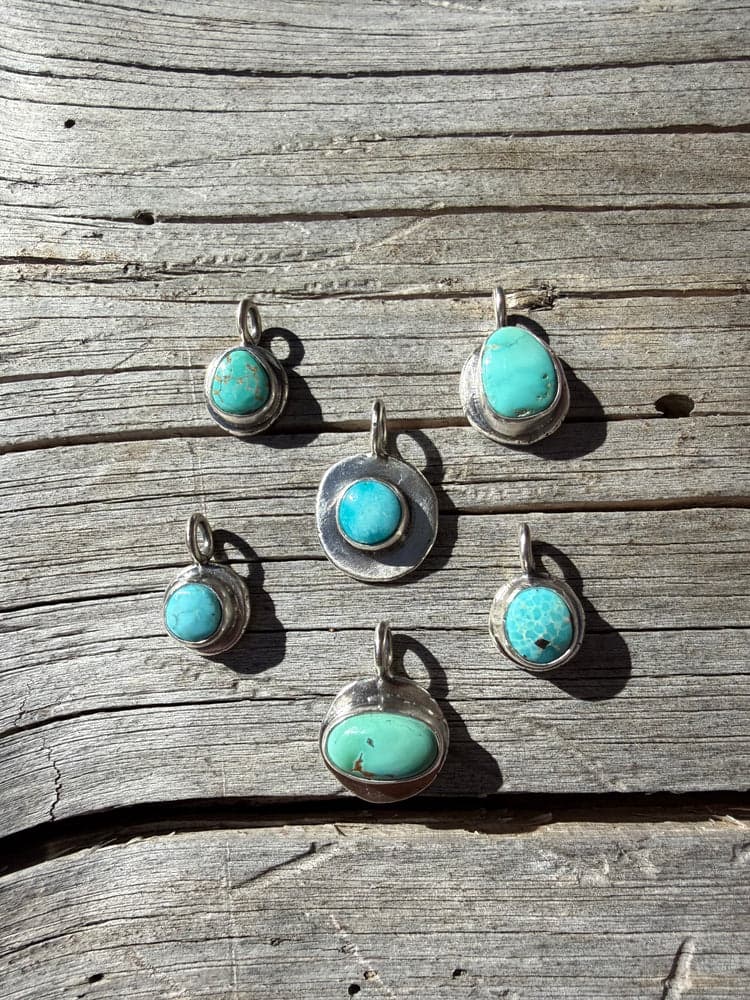 Six silver and turquoise pendants arranged in a cluster on rustic wood