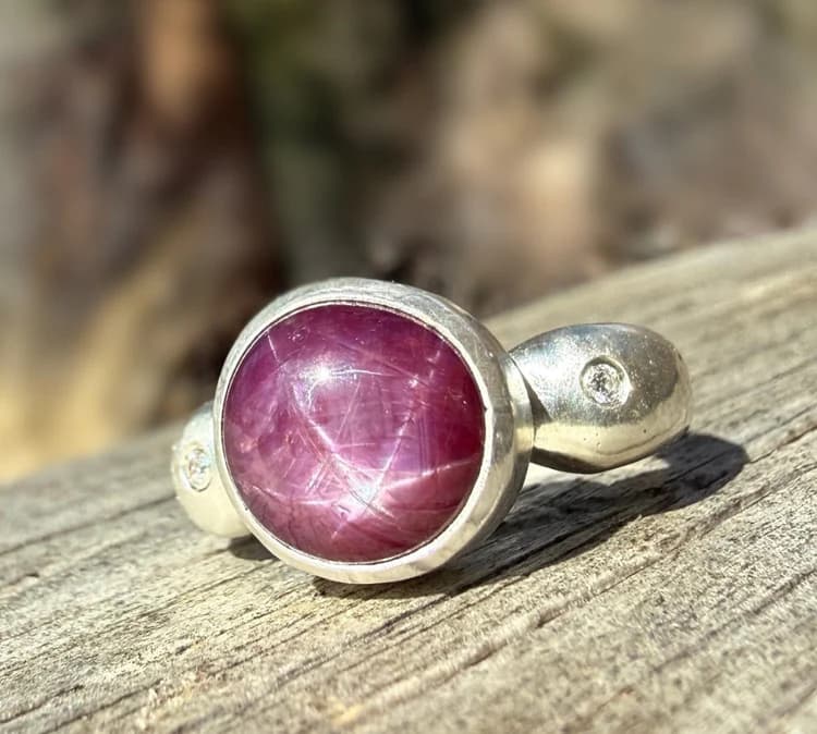 Handmade silver ring with a round star ruby cabochon and side accents on grey wood