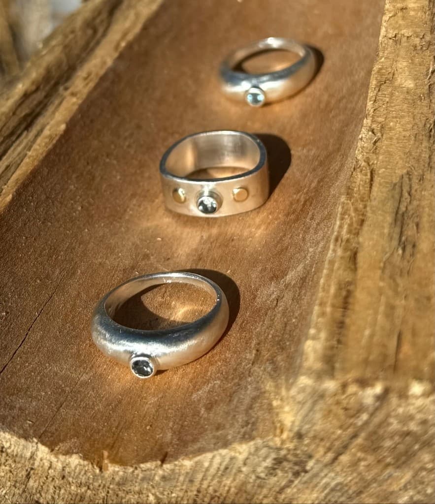 Three silver rings with small blue-green stones in a line on textured wood