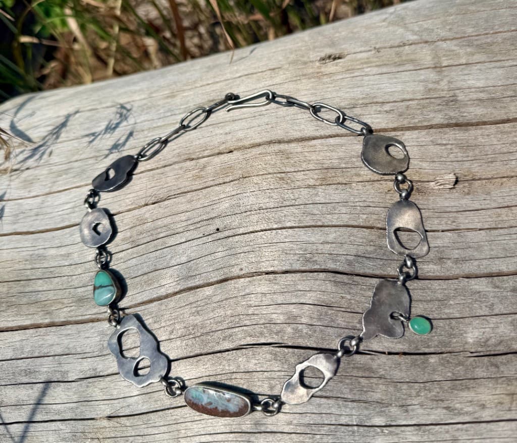 Sterling silver necklace with turquoise and accent stones laid on weathered driftwood