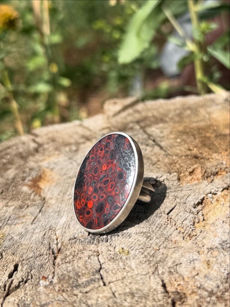 Handmade silver ring with a red patterned cabochon stone on weathered wood