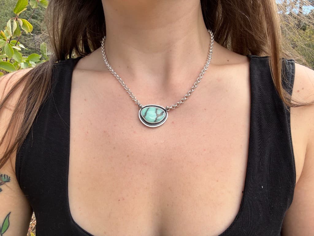Handmade silver necklace with an oval turquoise pendant worn against a black top