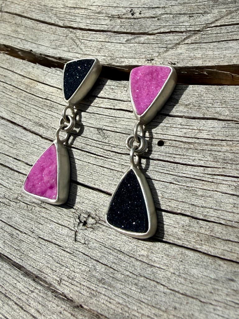 Handmade silver dangle earrings with triangular pink and black druzy stones on weathered wood