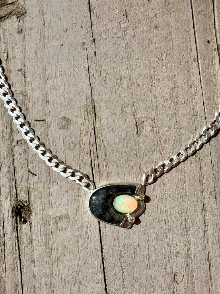 Handcrafted silver curb chain necklace with a pendant featuring a fiery opal and accent stones on weathered wood