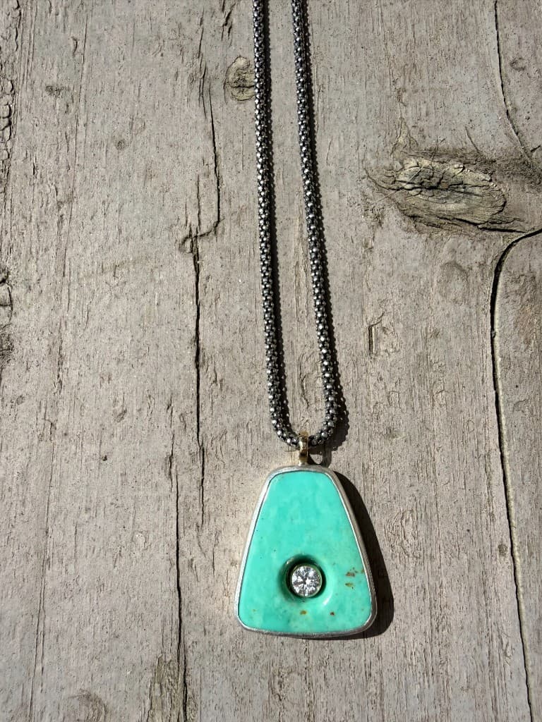 Oxidized silver popcorn chain with a turquoise trapezoid pendant and gold bail on weathered grey wood