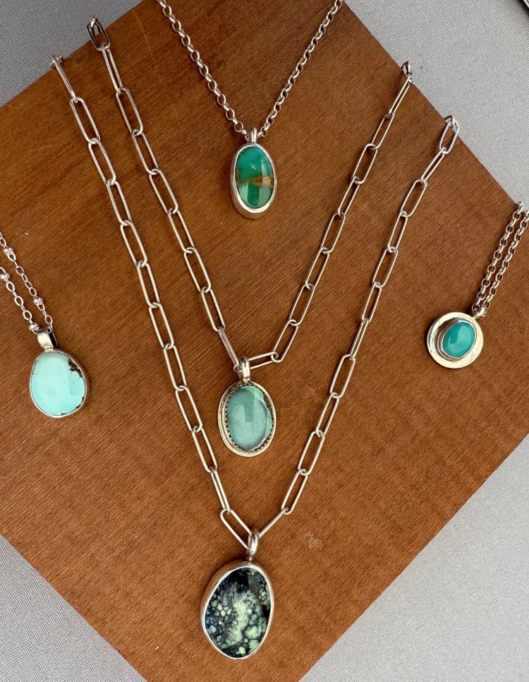 Five silver necklaces with turquoise pendants on a wooden block