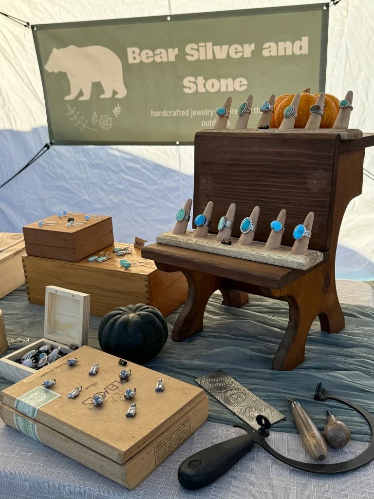 Bear Silver & Stone booth at an outdoor market with rings and turquoise on wooden displays